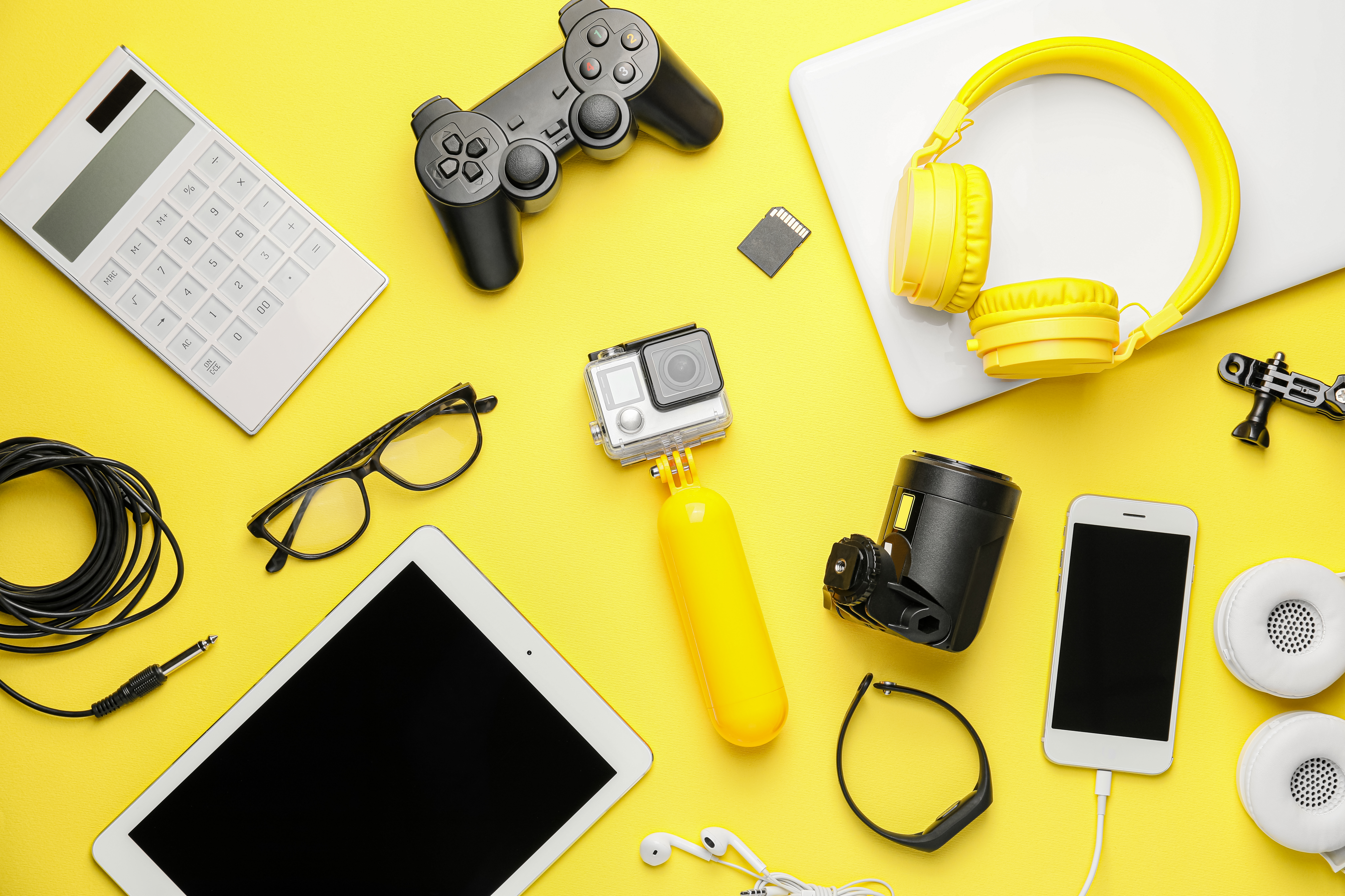 An assortment of gadgets on a yellow background with a GoPro camera on a yellow selfie stick in the middle