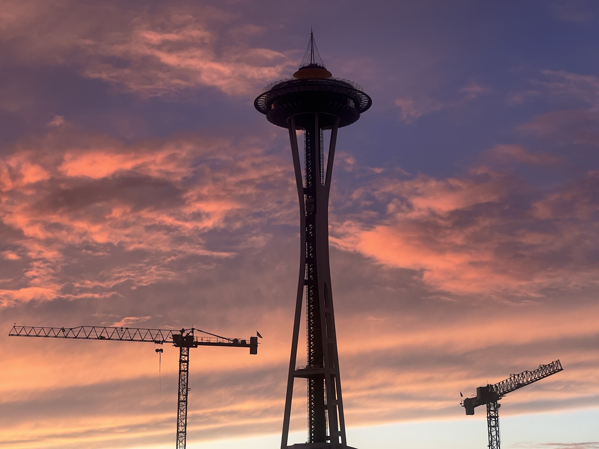 Space Needle in Seattle with construction cranes in the background and clouds in the sky at sunset