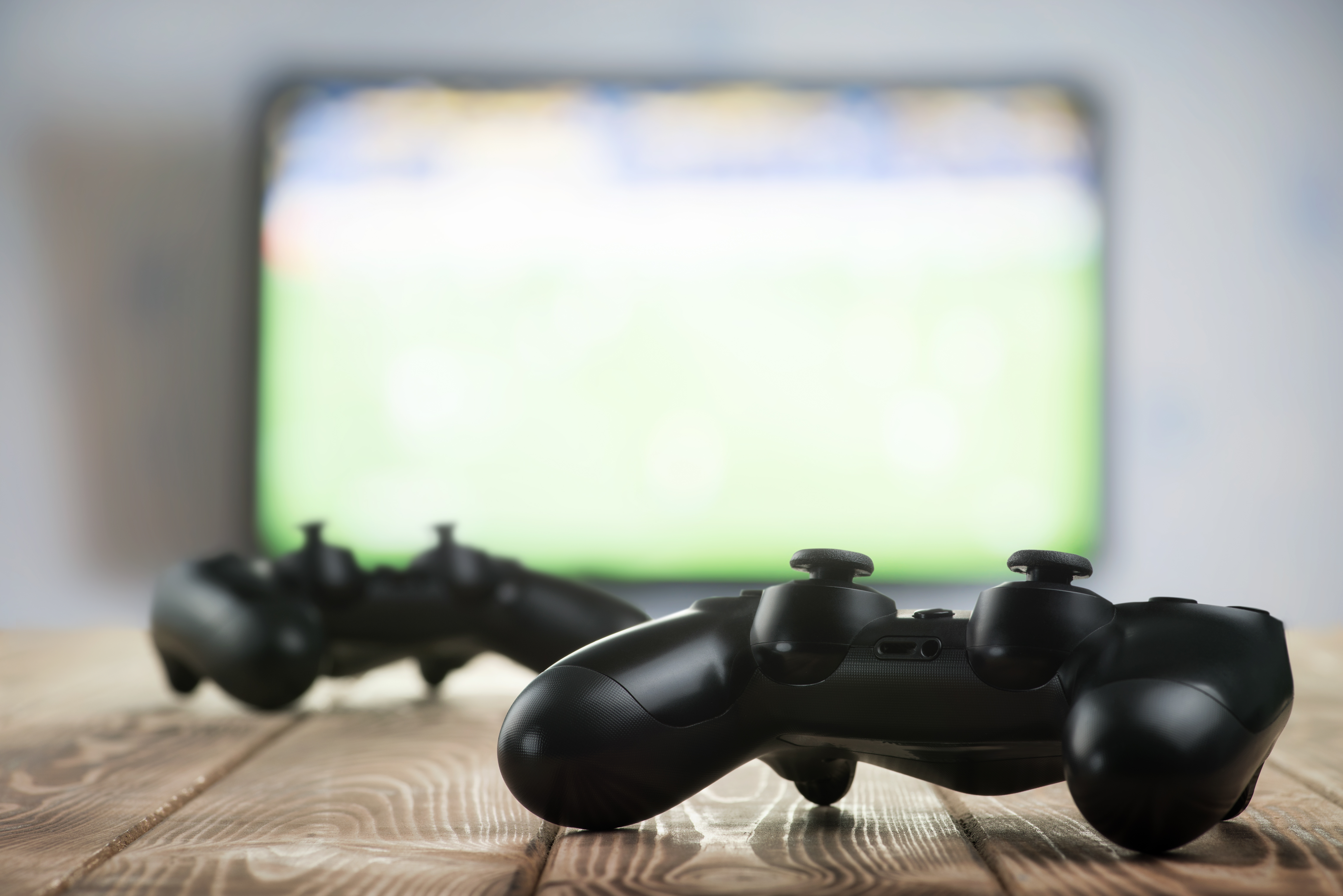 Close up view of two game controllers sitting on a wooden table with a blurred out TV screen in the background